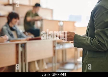 Mano di giovane insegnante fiduciosa in giacca verde scuro che fa rapporto descrivendo i punti principali del seminario o della lezione agli studenti Foto Stock