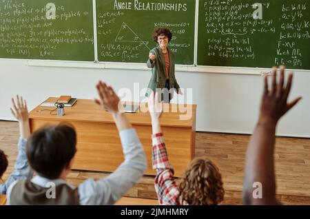 Insegnante di successo che punta ad uno degli studenti interrazziali alzando le mani che desiderano fare o rispondere alle domande dopo la presentazione del nuovo soggetto Foto Stock