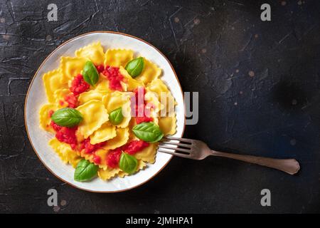 Ravioli con salsa di pomodoro e basilico su piatto, top shot con forchetta Foto Stock