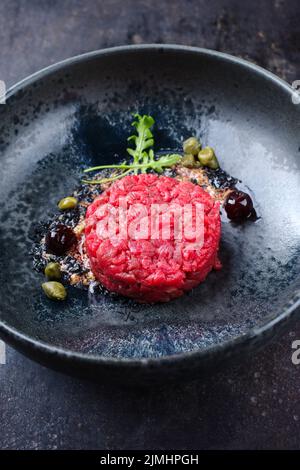 Tartaro gourmet in stile moderno grezzo da filetto di manzo con capperi e amarena ciliegia servito con crema al tartufo e lattuga come primo piano in un disegno nordico pl Foto Stock