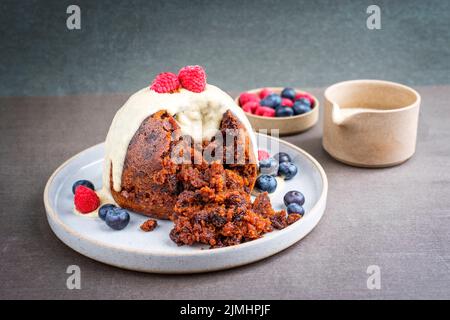 Budino tradizionale australiano di prugne come primo piano con frutta e salsa di rum alla vaniglia su un piatto da dessert dal design moderno con spazio copia Foto Stock