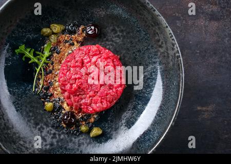 Tartaro gourmet in stile moderno crudo di filetto di manzo con capperi e amarena ciliegia servito con crema al tartufo e lattuga come vista dall'alto Foto Stock