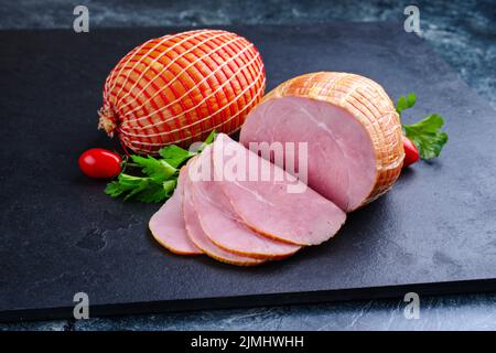 Tradizionale prosciutto di Pasqua tedesco bollito con pomodori e prezzemolo offerto come primo piano su una tavola nera con spazio copia Foto Stock