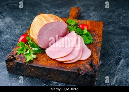 Tradizionale prosciutto di Pasqua tedesco bollito con pomodori e prezzemolo offerto come primo piano su un vecchio rustico bordo di legno con spazio copia Foto Stock