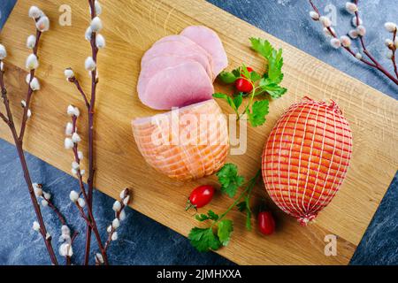 Tradizionale prosciutto di Pasqua tedesco bollito con pomodori e uova offerti come vista dall'alto su un moderno asse di legno di design Foto Stock