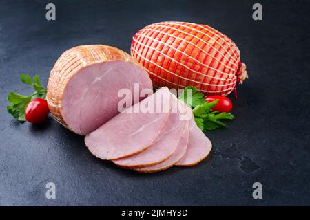 Tradizionale prosciutto di Pasqua tedesco bollito con pomodori e prezzemolo offerto come primo piano su una tavola nera con spazio copia Foto Stock