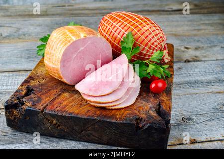 Tradizionale prosciutto di Pasqua tedesco bollito con pomodori e prezzemolo offerto come primo piano su un vecchio rustico bordo di legno con spazio copia Foto Stock