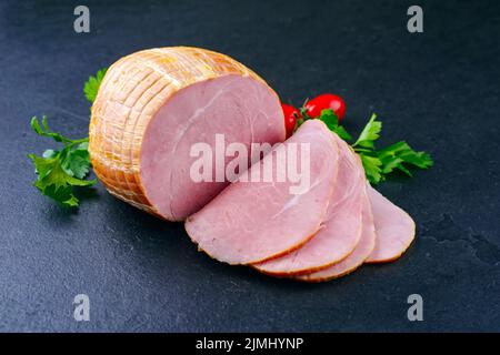 Tradizionale prosciutto di Pasqua tedesco bollito con pomodori e prezzemolo offerto come primo piano su una tavola nera con spazio copia Foto Stock