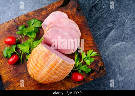 Tradizionale prosciutto di Pasqua tedesco bollito con pomodori e prezzemolo offerto come vista dall'alto su un vecchio rustico bordo di legno con spazio copia Foto Stock