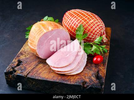 Tradizionale prosciutto di Pasqua tedesco bollito con pomodori e prezzemolo offerto come primo piano su un vecchio rustico bordo di legno con spazio copia Foto Stock