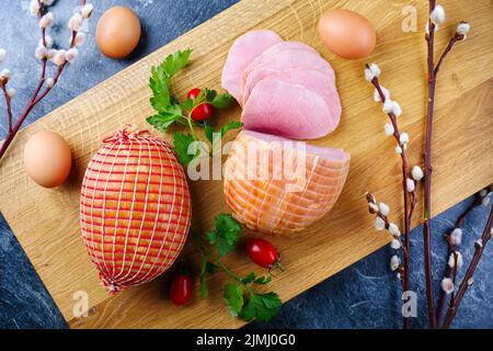 Tradizionale prosciutto di Pasqua tedesco bollito con pomodori e uova offerti come vista dall'alto su un moderno asse di legno di design Foto Stock