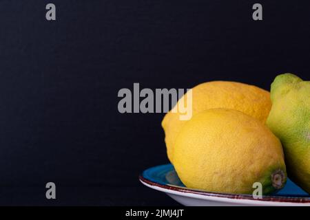 Primo piano di limoni su un piatto blu su sfondo nero Foto Stock