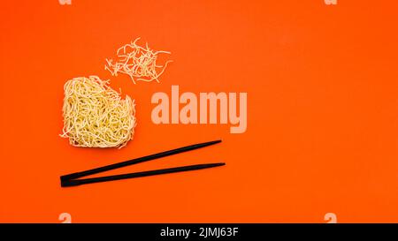 Spaghetti secchi e istantanei rotti con bacchette fondo arancione Foto Stock
