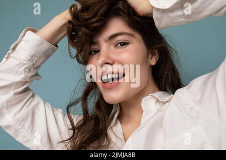 Ritratto di bella positiva allegra carina sorridente giovane donna brunette in casual camicia bianca isolato su sfondo blu con Foto Stock