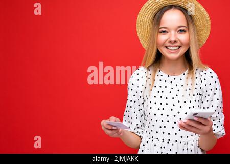 Foto di giovane bella bella bella donna felice sorridente bionda vestito casual e cappello di paglia isolato su sfondo rosso wi Foto Stock