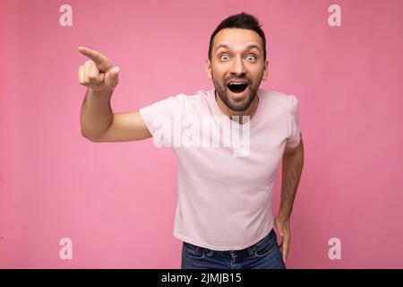 Foto di un bell'emotivo felice uomo brunetto stupito in casual t-shirt rosa isolato su sfondo rosa con spazio copia Foto Stock