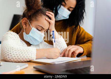 Bambina casa indossare maschera medica durante la scuola online con la sorella grande Foto Stock