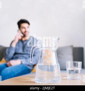 Caraffa in vetro vicino all'uomo con smartphone Foto Stock