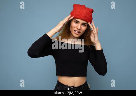 Giovane emotivo insoddisfatto bella donna brunette ricci con emozioni sincere indossando elegante crop nero top e cappello rosso isolat Foto Stock