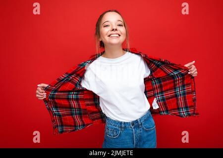 Giovane bella donna in elegante camicia rossa hipster e casual t-shirt bianca per mockup. La femmina positiva mostra emozioni facciali. F Foto Stock