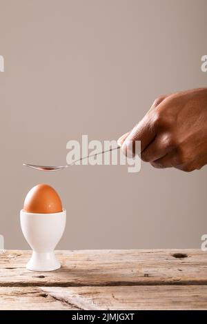 Cucchiaino di tenuta tagliato a mano sopra l'uovo bollito marrone in tazza su sfondo grigio con spazio di copia Foto Stock