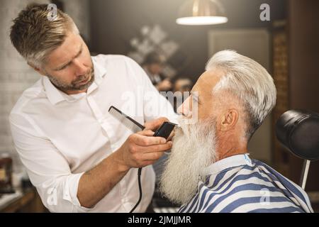 Bell'uomo anziano che ottiene styling e rifilatura della sua barba Foto Stock