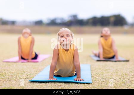 Le studentesse multirazziali elementari che fanno il cane rivolto verso l'alto pongono l'esercizio sul tappeto yoga Foto Stock