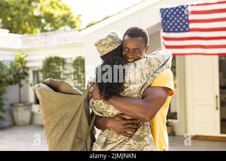 Donna, adulto medio, soldato afroamericano che abbraccia marito sorridente all'arrivo a casa Foto Stock