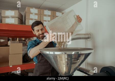 L'imprenditore versa i chicchi di caffè crudo in una moderna tostatrice. Foto Stock