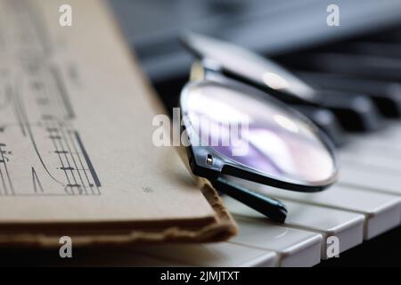 Spartiti musicali e occhiali sui tasti del pianoforte Foto Stock