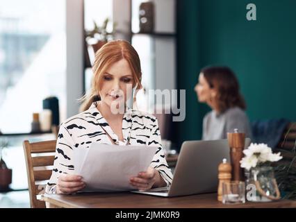 Vorrei fare un doppio controllo: Una donna di mezza età attraente che fa i documenti mentre si siede all'interno di un bar durante il giorno. Foto Stock