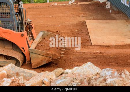 Piccolo trattore che lavora con la terra che si sposta verso il livellamento del terreno vicino a casa nuova Foto Stock