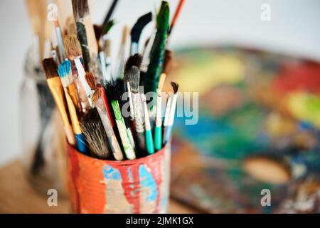 Lets get painting. Una lattina piena di pennelli in uno studio d'arte vuoto dopo una lezione di pittura. Foto Stock