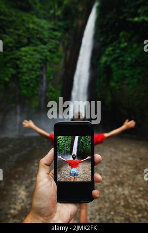 Uomo che fotografa la sua ragazza accanto alla bella cascata Foto Stock