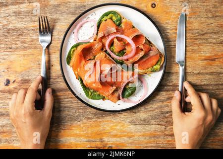 Mani femminili e toast deliziosi con salmone affumicato, avocado e foglie di basilico Foto Stock