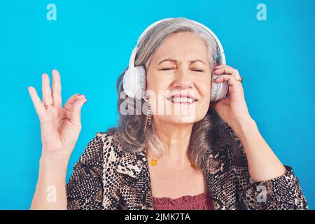 Questa canzone mi riporta ai bei vecchi tempi. Una donna funky e allegra che ascolta la musica sulle cuffie su sfondo blu. Foto Stock