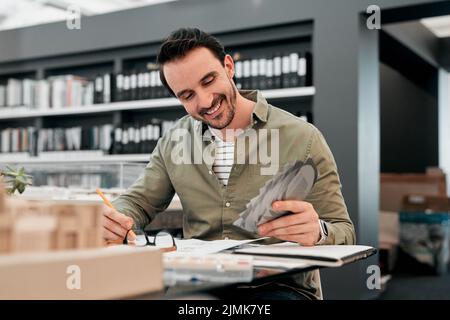 Ogni cosa che si unisca proprio come ho previsto. Un bel giovane architetto maschile sorridendo mentre lavorava con alcuni progetti in un ufficio moderno. Foto Stock