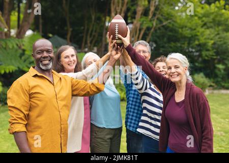 Ritratto di sorridente multirazziale attivo senior maschile e femminile amici tenendo palla di rugby in cortile Foto Stock