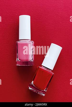 Bottiglie di smalto per unghie rosse e rosa su sfondo rosso, manicure e cosmetici di bellezza Foto Stock