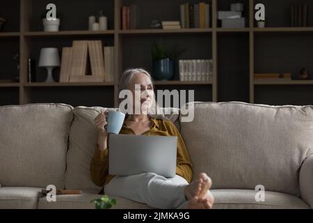 Felice sognante pensiva donna in pensione rilassarsi sul comodo divano Foto Stock