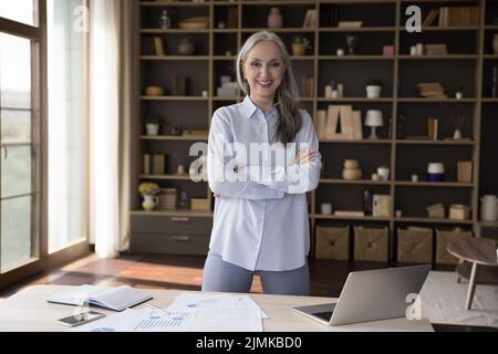 Donna d'affari anziana e sicura in piedi al tavolo di lavoro Foto Stock