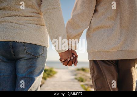 Romantica coppia senior che tiene le mani mentre si cammina lungo una passerella sulla spiaggia. Coppia anziana irriconoscibile che prende una vacanza al mare rinfrescante af Foto Stock