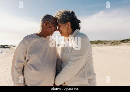 Una coppia di anziani sorridendo e toccando la testa insieme in spiaggia. Coppia anziana allegra che condivide un momento romantico all'aperto. Buona coppia Foto Stock
