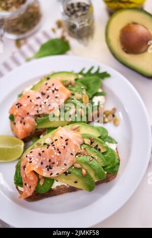 Avocado appena fatto, salmone e formaggio cremoso toast su un piatto di ceramica bianca Foto Stock