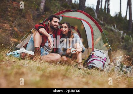 Una giovane coppia affettuosa che si unisce a una vacanza in campeggio. Coppia seduta insieme di fronte alla loro tenda. Foto Stock