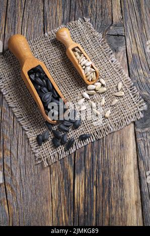 Semi di girasole sbucciati e non sbucciati in una paletta di legno su un vecchio sfondo di legno. Semi di girasole sbucciati e sbucciati in una paletta sul retro di legno vecchio Foto Stock