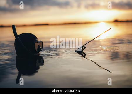 Subacqueo per la pesca d'altura che tiene un fucile mentre è immerso in acqua di mare al tramonto. Avventuroso subacqueo a caccia di pesci nel mezzo dell'oceano. Foto Stock