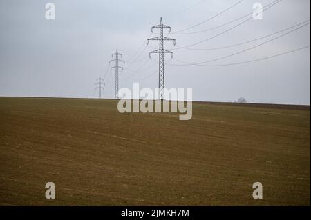 Una linea ad alta tensione passa su un campo calvo. Le nuvole grigie di nebbia rafforzano l'impressione del paesaggio. Foto Stock