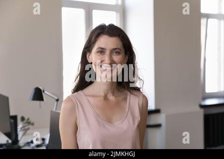 Donna d'affari sorridente che si posa in un ambiente di lavoro moderno, ritratto a testa girata Foto Stock