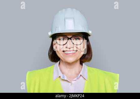 Lavoratrice industriale femminile in elmetto protettivo e gilet su sfondo grigio Foto Stock